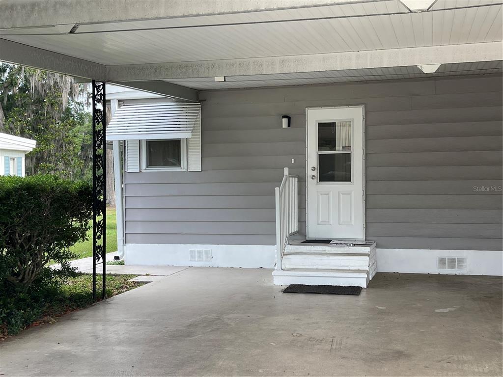 A gray-sided home features a white door, concrete carport, and a small set of stairs — 87 N BOBWHITE ROAD, WILDWOOD, FL