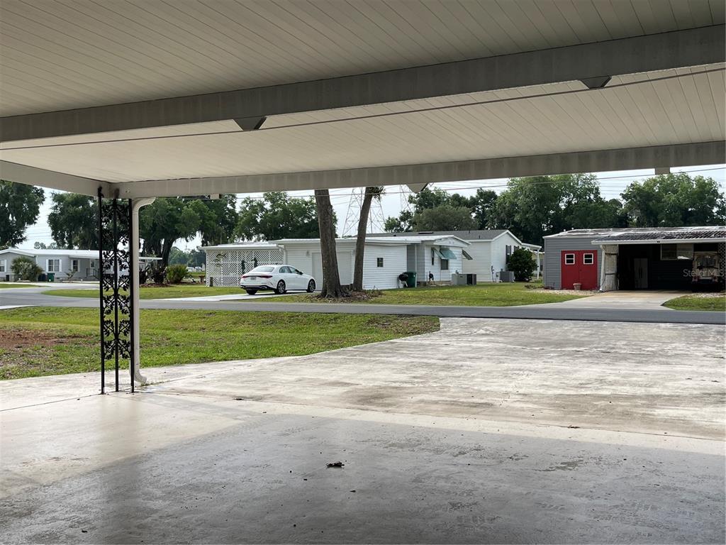 A view from a covered carport looking out toward a street and neighboring houses — 87 N BOBWHITE ROAD, WILDWOOD, FL