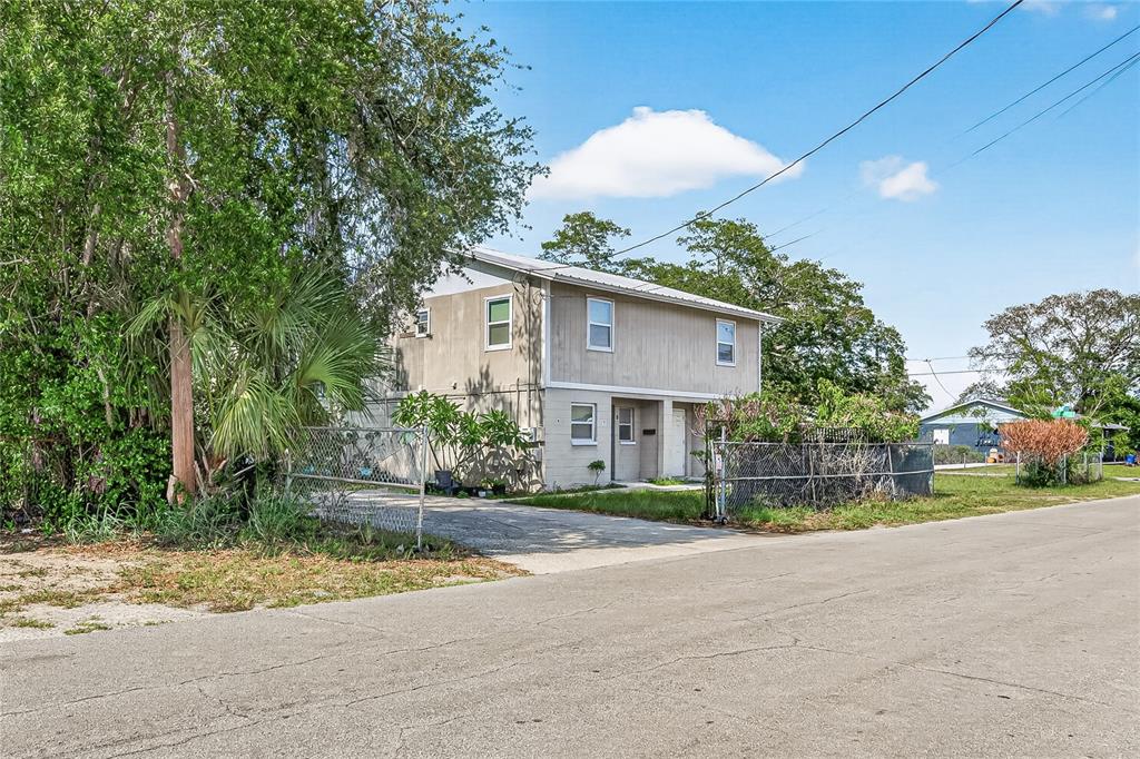 A two-story beige house with a metal roof sits behind a chain-link fence — 3602 N 54TH STREET, TAMPA, FL
