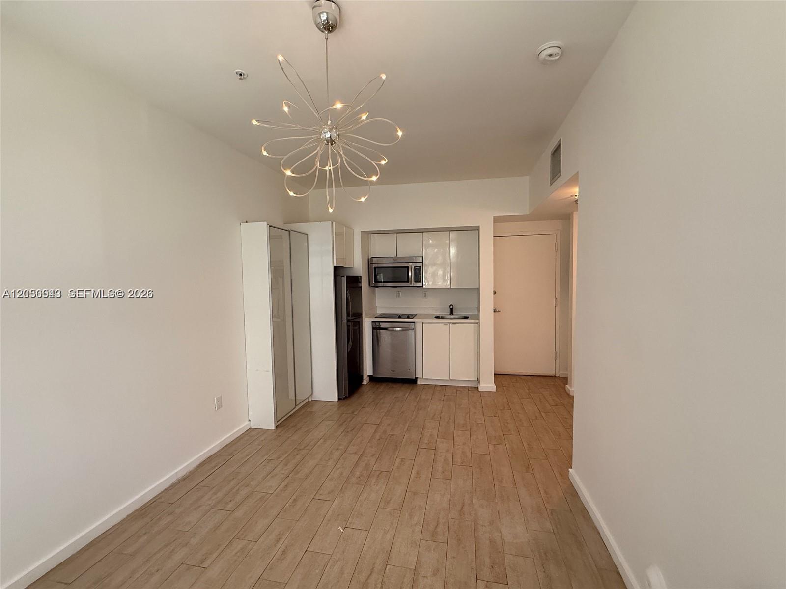 A small kitchen features white cabinets, stainless steel appliances, and a modern sputnik chandelier — 1611 Meridian Ave # 202, Miami Beach FL 33139, MIAMI BEACH, FL