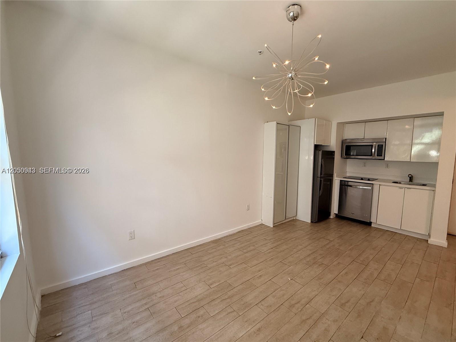 A kitchen and dining area features white cabinets, stainless steel appliances, and wood-look tile flooring — 1611 Meridian Ave # 202, Miami Beach FL 33139, MIAMI BEACH, FL