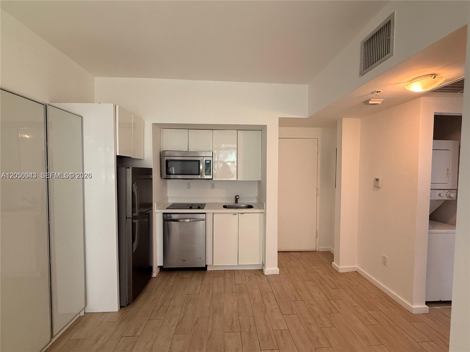 A small kitchen features white cabinets, stainless steel appliances, and light wood-look tile flooring — 1611 Meridian Ave # 202, Miami Beach FL 33139, MIAMI BEACH, FL