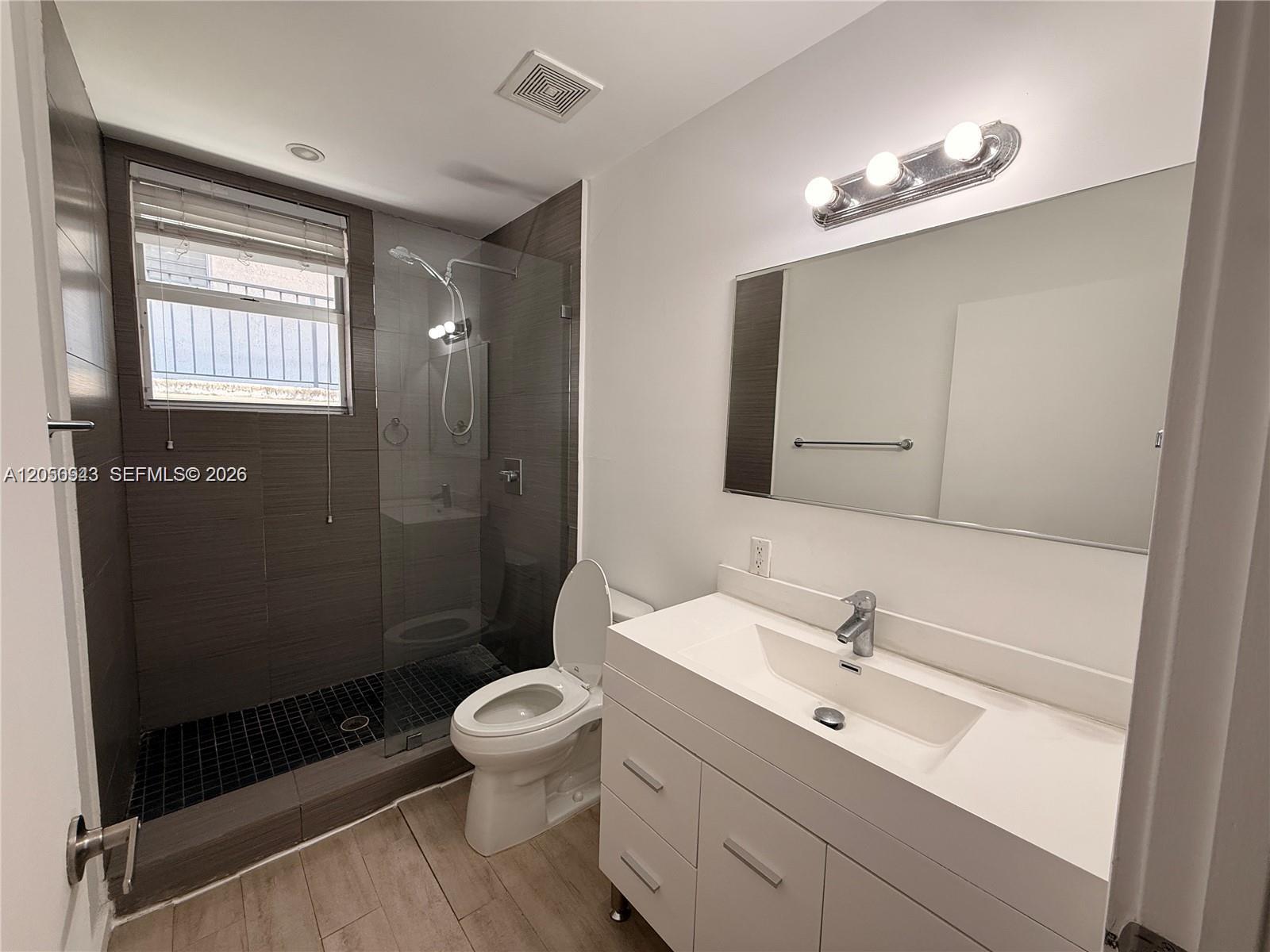 A modern bathroom features a glass-enclosed walk-in shower, a white vanity, and wood-look flooring — 1611 Meridian Ave # 202, Miami Beach FL 33139, MIAMI BEACH, FL
