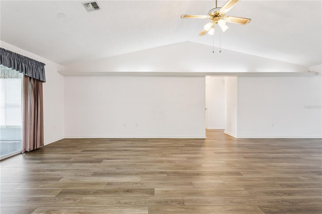 A spacious living room with wood-look flooring, a vaulted ceiling, and an open kitchen area — 32 GORDON COURT, LEESBURG, FL