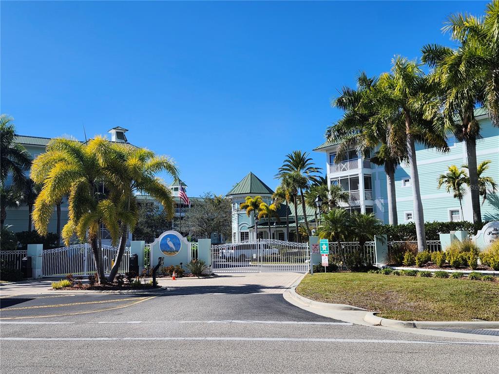 A gated entrance leads to a multi-story residential complex with palm trees and blue skies — 5127 MELBOURNE STREET UNIT F103, PUNTA GORDA, FL