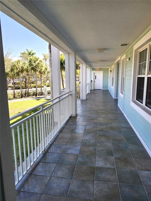 A long, covered outdoor balcony features tiled flooring, white railings, and light blue siding — 5127 MELBOURNE STREET UNIT F103, PUNTA GORDA, FL