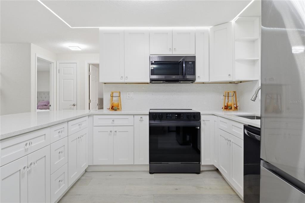 A modern kitchen features white cabinets, black appliances, and light-colored countertops — 6338 ABERDEEN AVENUE, NEW PORT RICHEY, FL