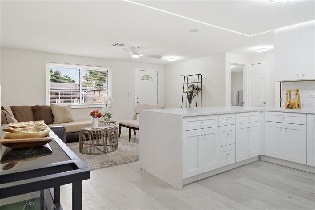 A modern open-concept kitchen with white cabinets and quartz countertops overlooks a living area — 6338 ABERDEEN AVENUE, NEW PORT RICHEY, FL
