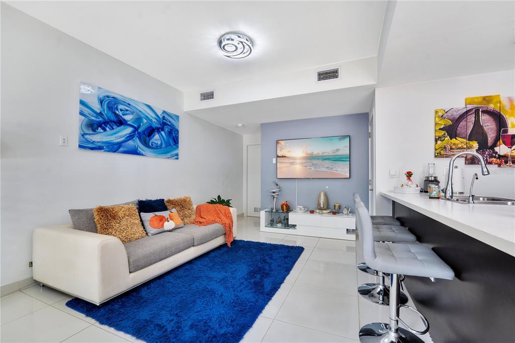A modern living room features a white sofa, blue area rug, and an open kitchen — 13938 SW 259 WAY, HOMESTEAD, FL