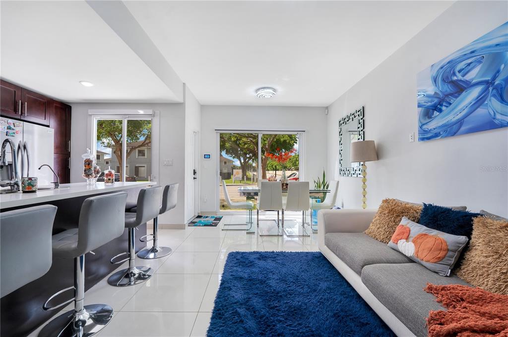 A modern open-concept living room and kitchen area with white tile flooring and sliding doors — 13938 SW 259 WAY, HOMESTEAD, FL