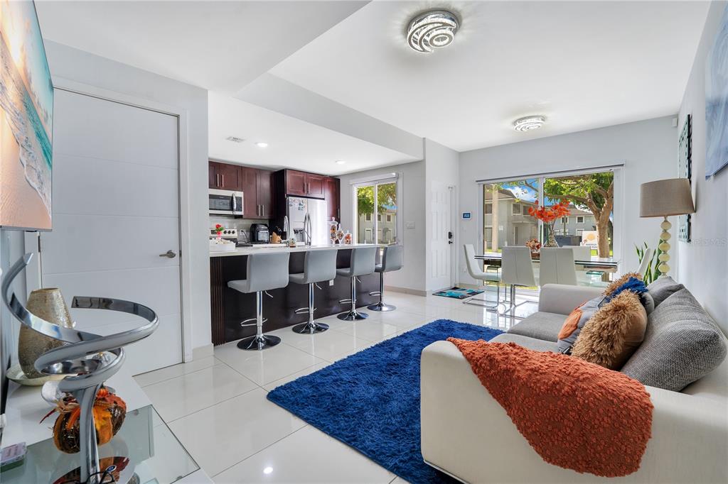 An open-concept living room and kitchen featuring white tile floors and a blue rug — 13938 SW 259 WAY, HOMESTEAD, FL