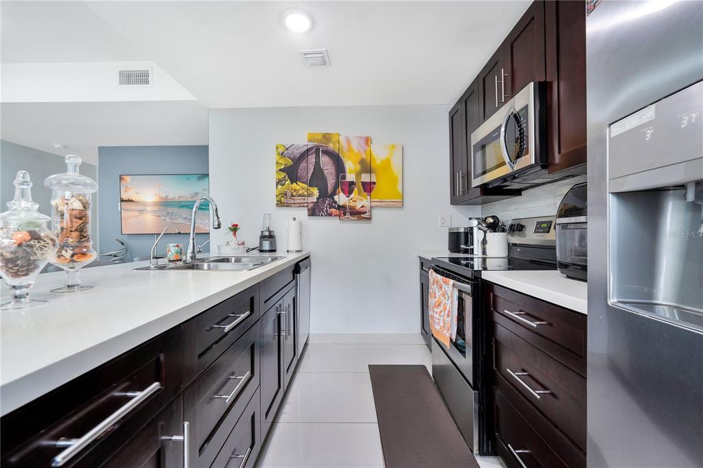 A modern kitchen features dark wood cabinets, white countertops, stainless steel appliances, and tile flooring — 13938 SW 259 WAY, HOMESTEAD, FL