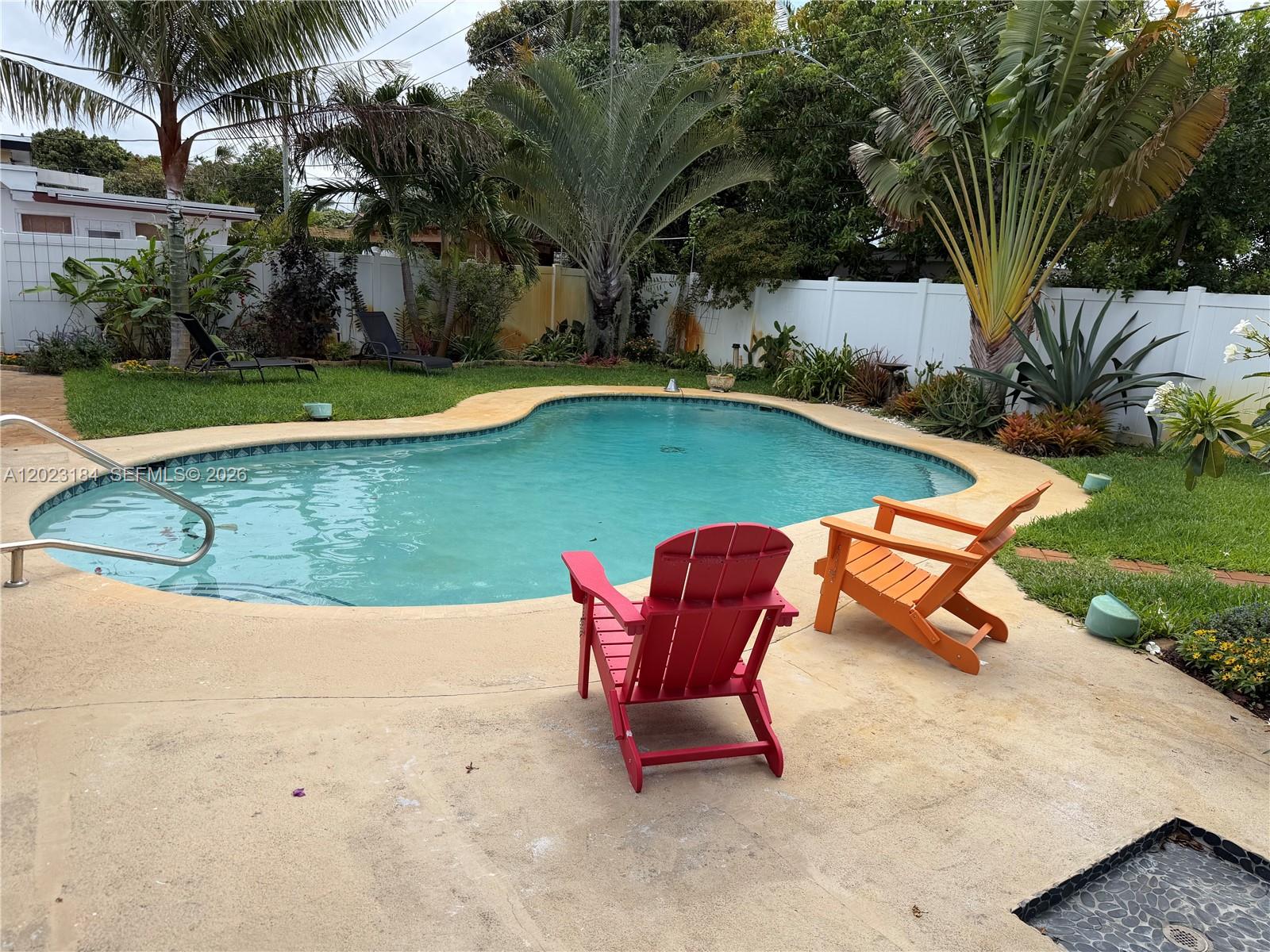 A backyard features a kidney-shaped swimming pool, two colorful Adirondack chairs, and lush tropical landscaping — 3837 NE 17th Ave, Pompano Beach FL 33064, POMPANO BEACH, FL
