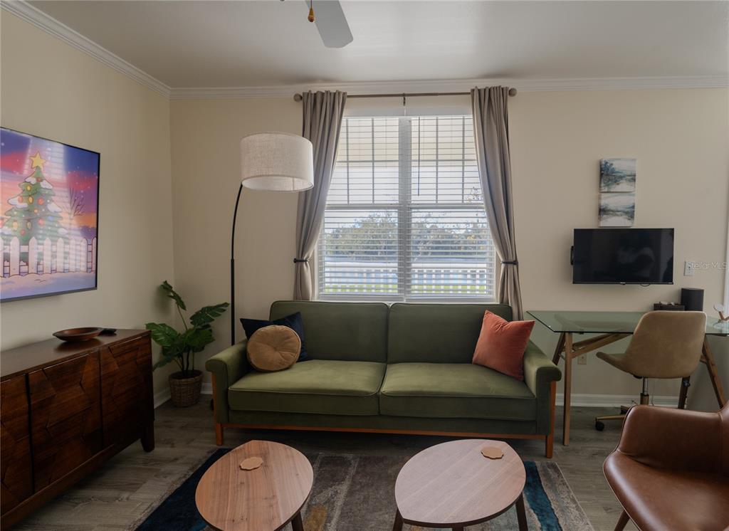 A living room features a green sofa, a glass desk, and a television on the wall — 770 SIENA PALM DRIVE UNIT 203, CELEBRATION, FL