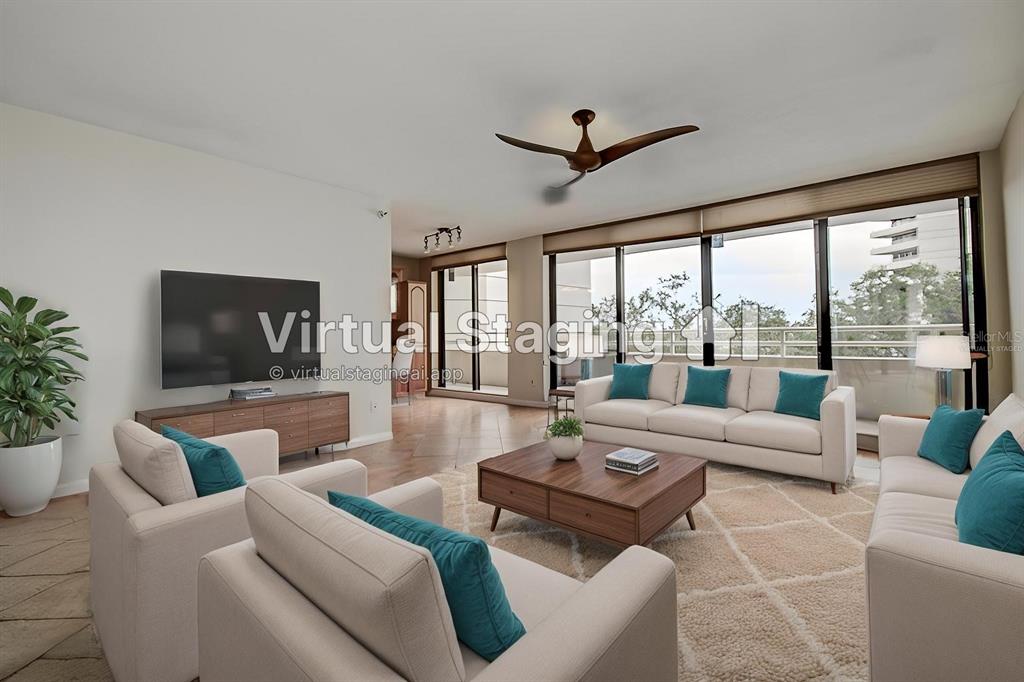 This virtually staged living room features a large sectional, armchairs, and floor-to-ceiling windows — 5940 PELICAN BAY PLAZA S UNIT 406, GULFPORT, FL