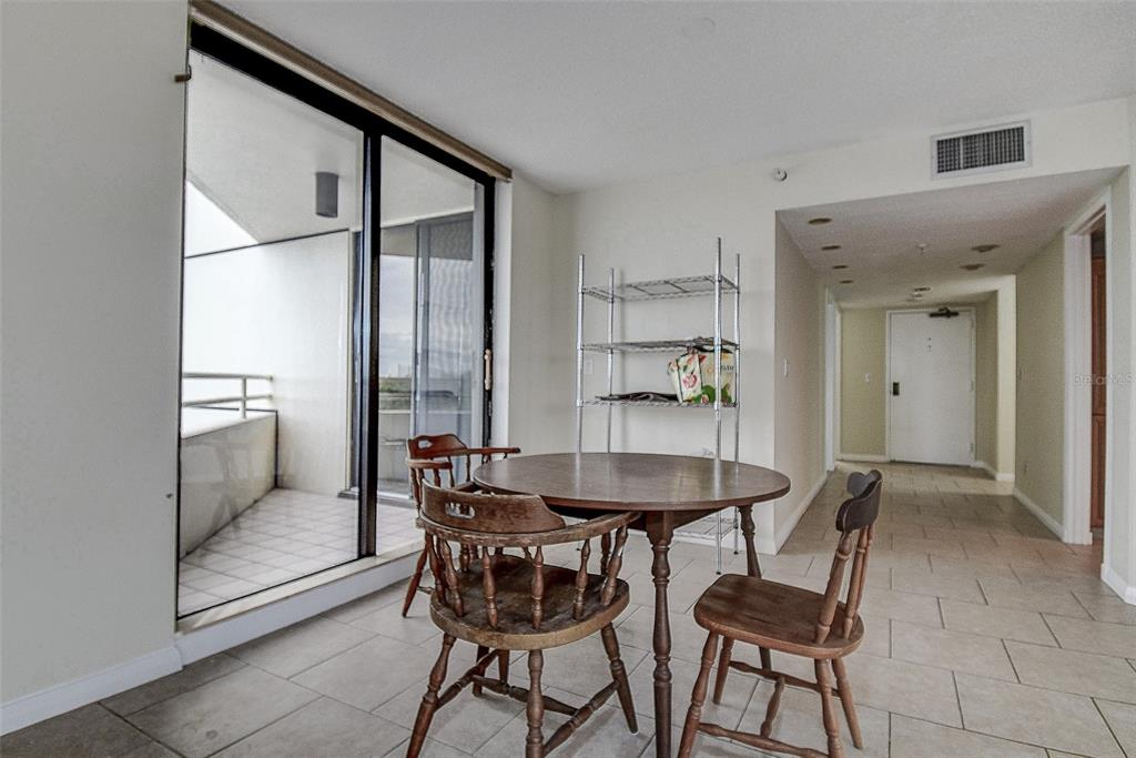 A dining area features a round wooden table, three chairs, metal shelving, and a balcony — 5940 PELICAN BAY PLAZA S UNIT 406, GULFPORT, FL