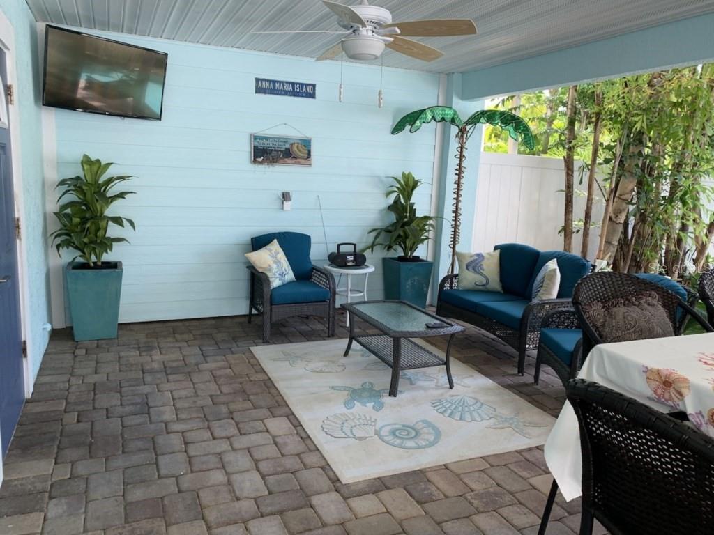 A covered patio features blue siding, wicker furniture, a patterned area rug, and a television — 303 62ND STREET UNIT A, HOLMES BEACH, FL