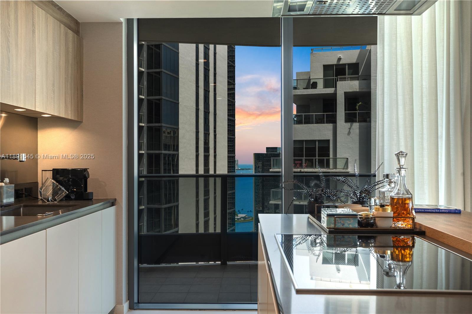 A modern kitchen features light wood cabinetry, a dark countertop, and a view of buildings — 1000 Brickell Plz # 3401, Miami FL 33131, MIAMI, FL