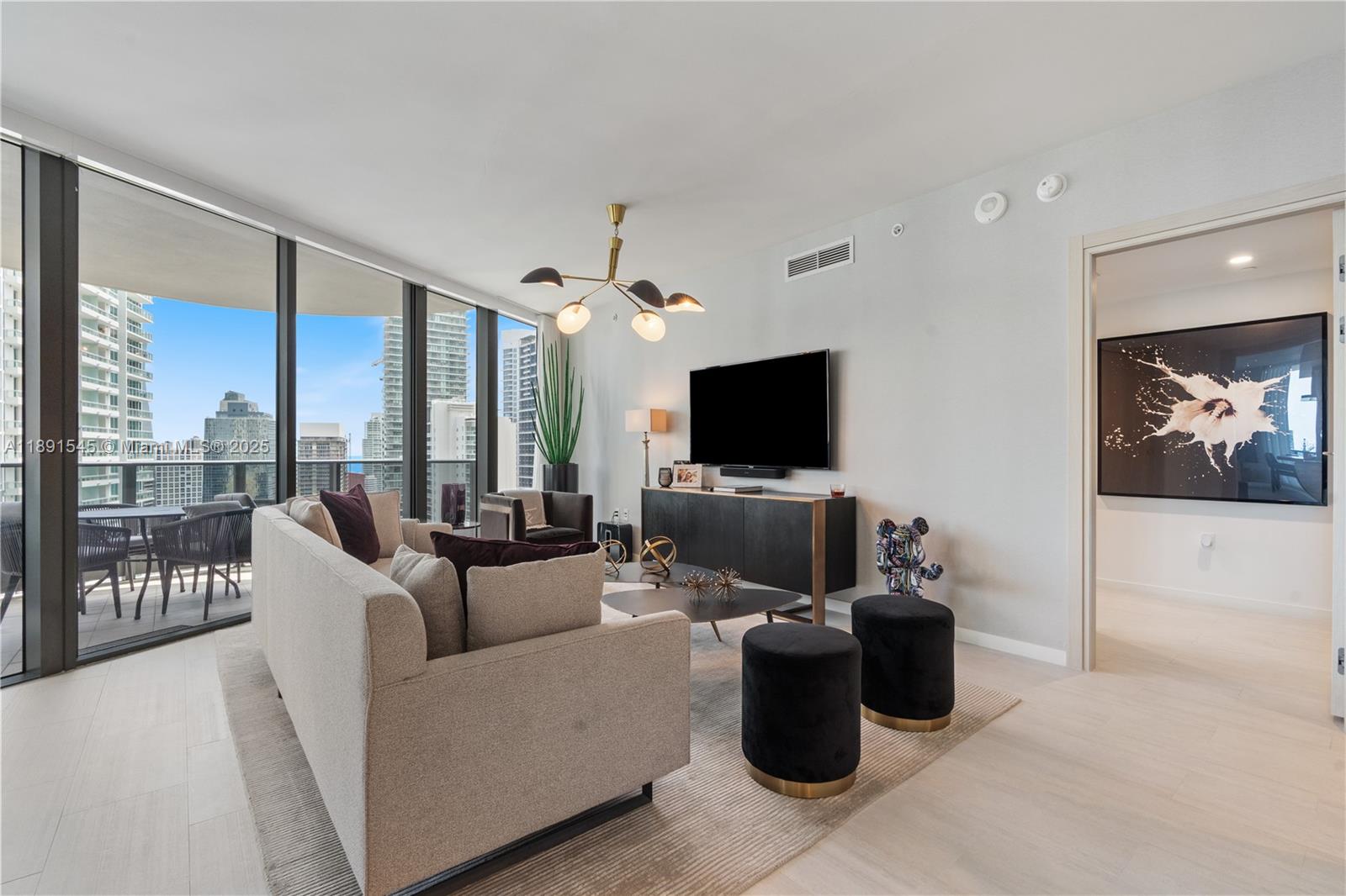 A modern living room features a beige sofa, black ottomans, and a balcony with city views — 1000 Brickell Plz # 3401, Miami FL 33131, MIAMI, FL