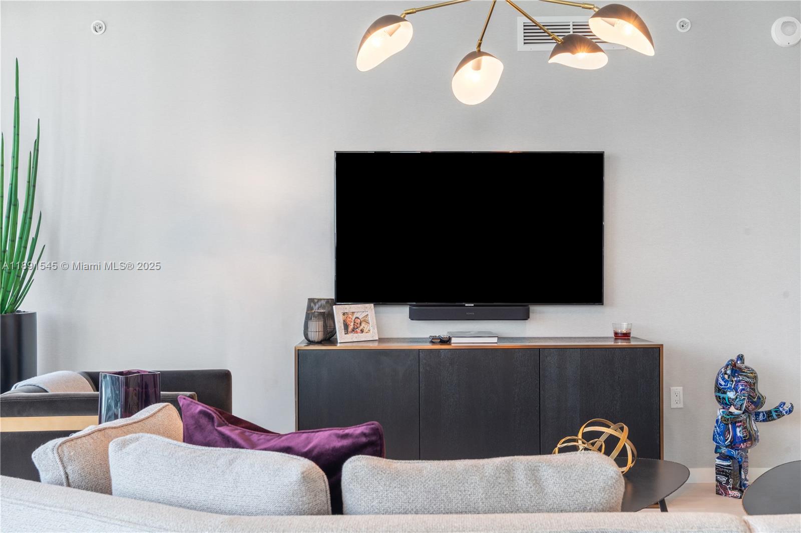 A living room features a wall-mounted television above a dark console and a modern chandelier — 1000 Brickell Plz # 3401, Miami FL 33131, MIAMI, FL