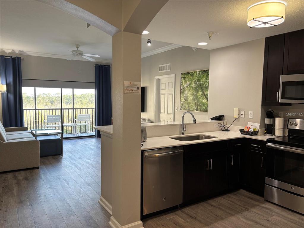 A kitchen with dark cabinets and stainless steel appliances overlooks a living area with a balcony — 14501 GROVE RESORT AVENUE UNIT 1503, WINTER GARDEN, FL