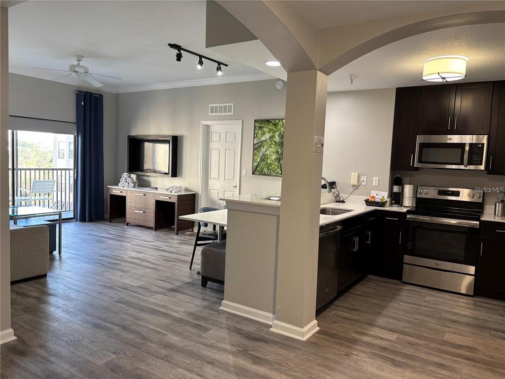 An open-concept kitchen and living area features dark wood cabinets, stainless steel appliances, and wood-look flooring — 14501 GROVE RESORT AVENUE UNIT 1503, WINTER GARDEN, FL