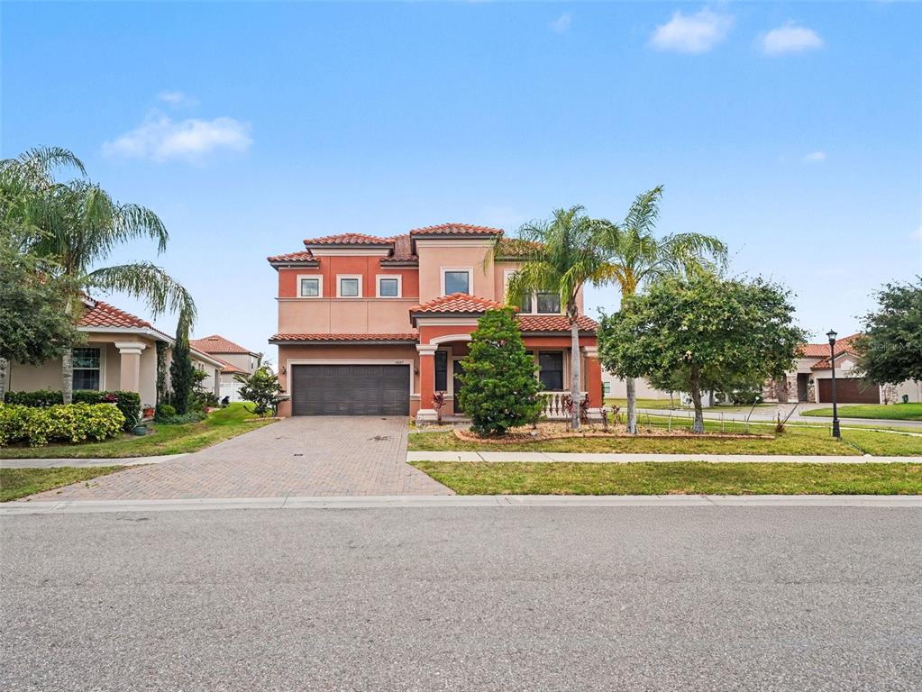 A two-story stucco house with a tile roof and a paved driveway under a blue sky — 12027 CARDINAL FLOWER DR, RIVERVIEW, FL