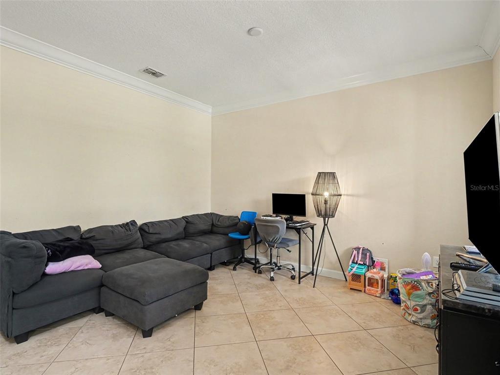 A living room features a large gray sectional sofa, a desk with a computer, and tile flooring — 12027 CARDINAL FLOWER DR, RIVERVIEW, FL
