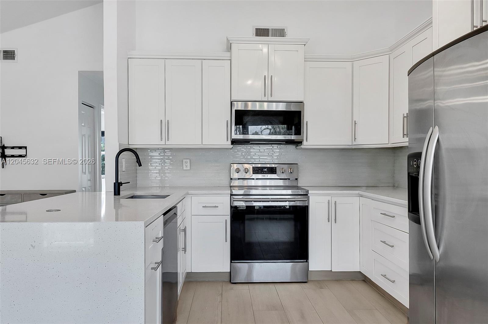 A modern kitchen features white cabinets, stainless steel appliances, and a quartz-topped island — 23384 Shetland Run, Boca Raton FL 33433, BOCA RATON, FL