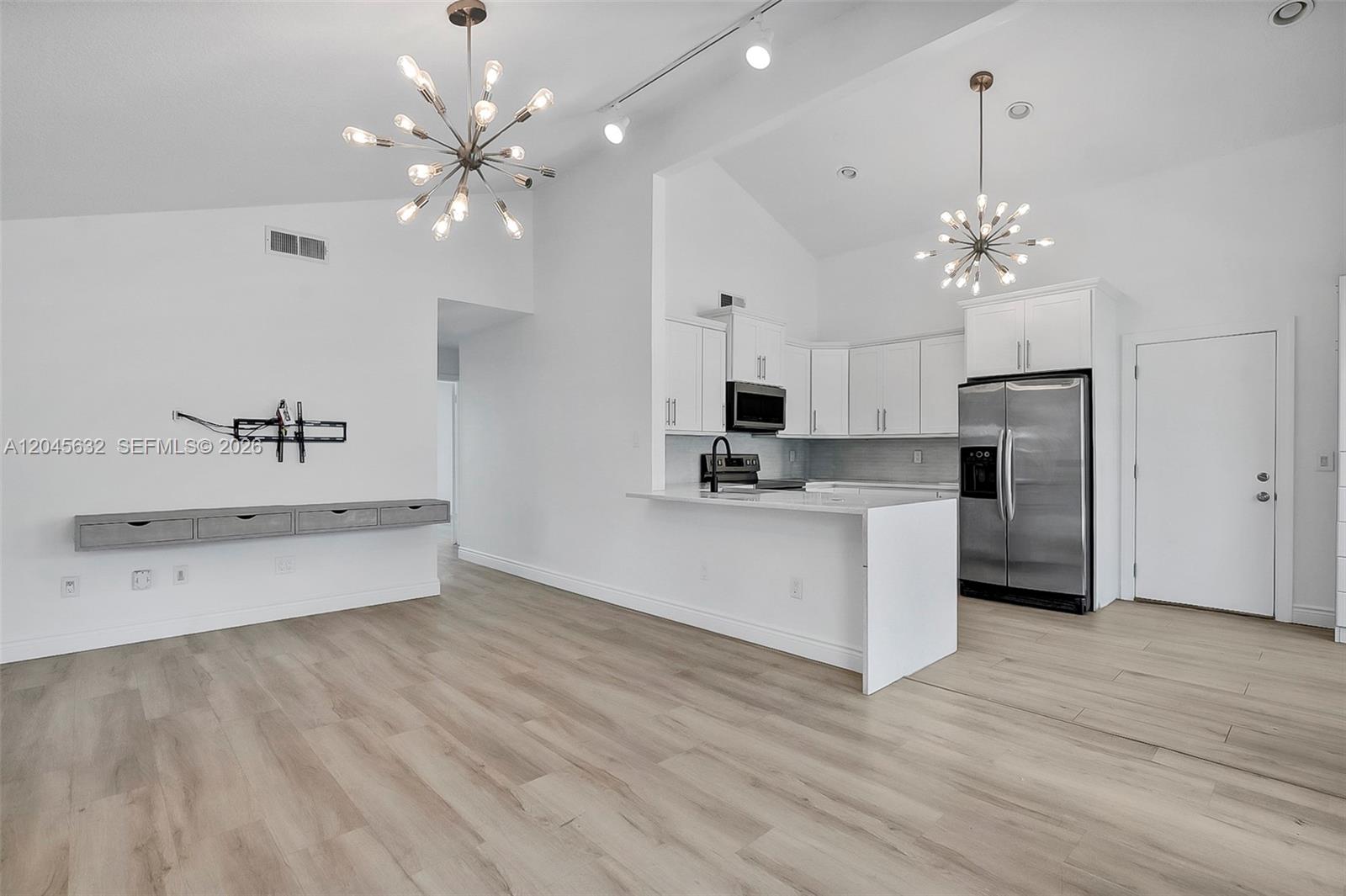 A bright, open-concept kitchen and living area features white cabinetry, stainless appliances, and light wood flooring — 23384 Shetland Run, Boca Raton FL 33433, BOCA RATON, FL