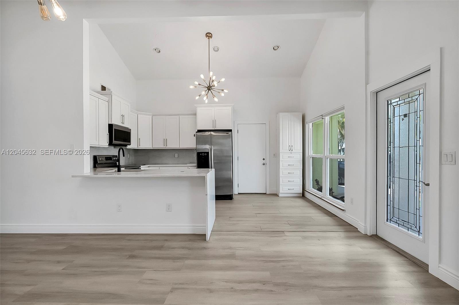 A modern kitchen features white cabinetry, stainless steel appliances, and light wood-look flooring — 23384 Shetland Run, Boca Raton FL 33433, BOCA RATON, FL
