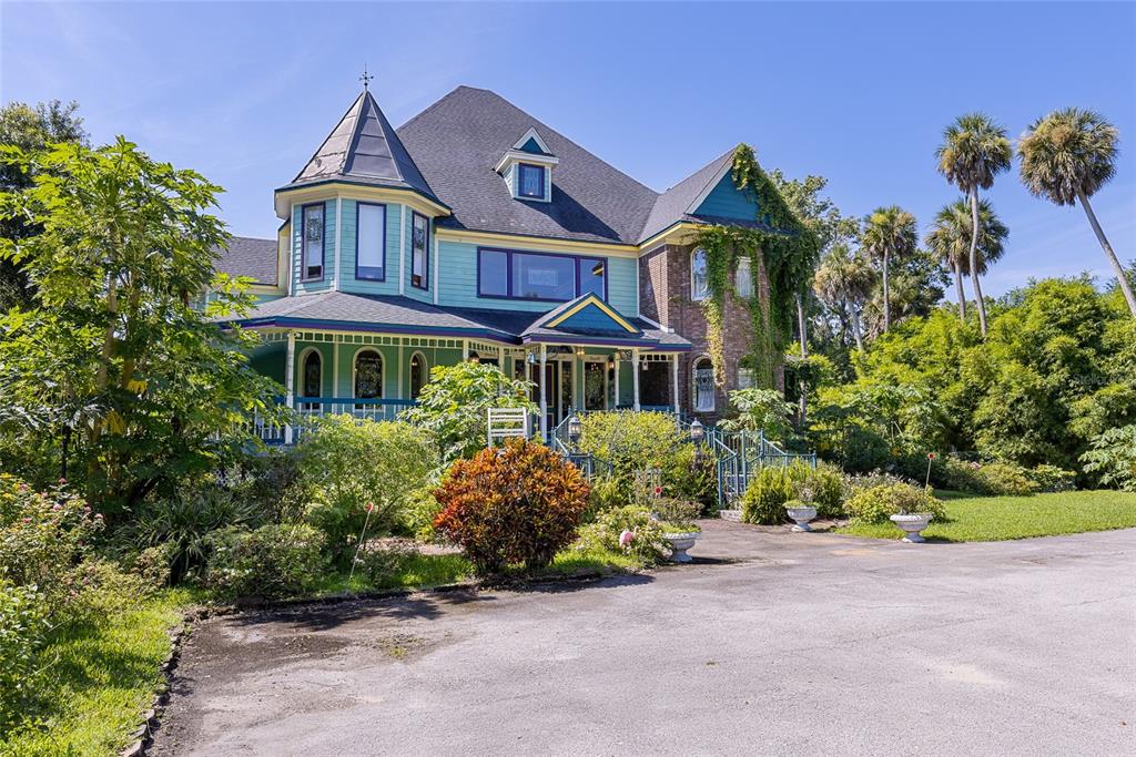 A multi-story Victorian-style house with a wraparound porch, turret, and lush landscaping — 6275 HALABRIN ROAD, HAINES CITY, FL