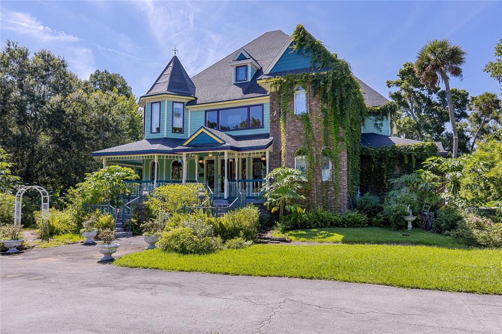 A large, multi-story Victorian-style house with a wraparound porch, brick accents, and lush landscaping — 6275 HALABRIN ROAD, HAINES CITY, FL
