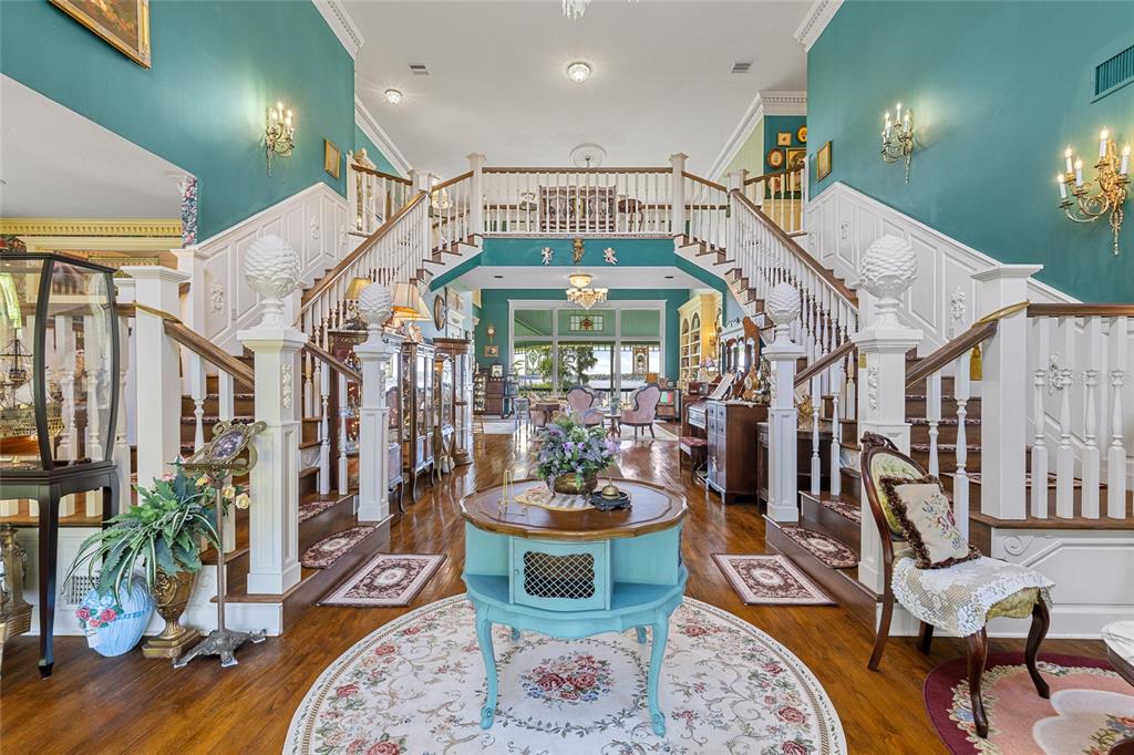 A grand foyer features a double staircase, teal walls, hardwood floors, and a central table — 6275 HALABRIN ROAD, HAINES CITY, FL