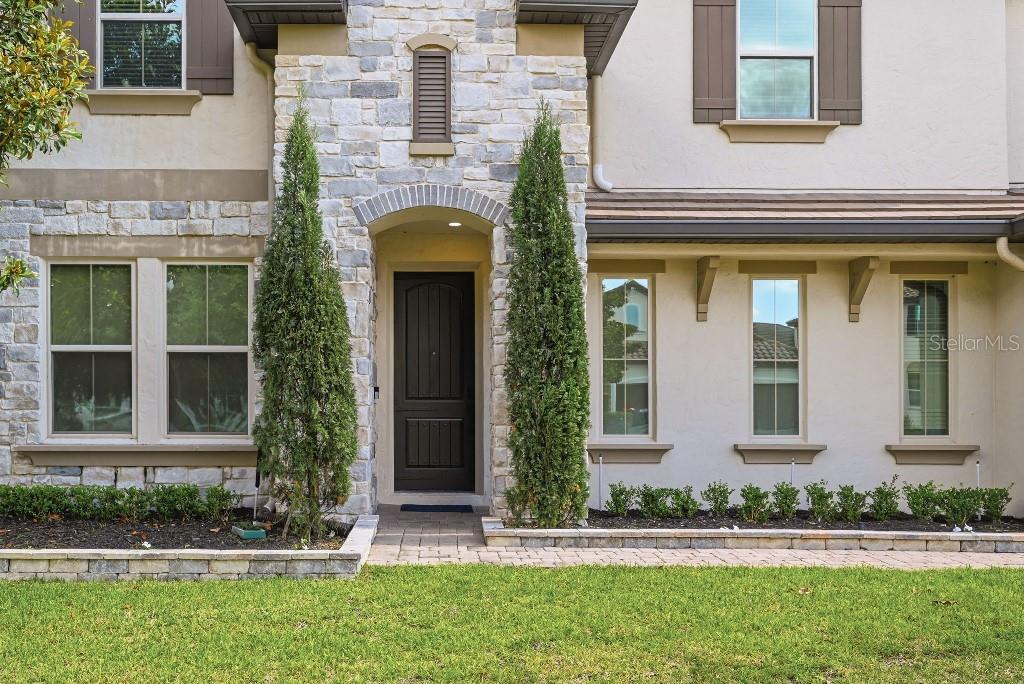 A stone-accented house exterior features a dark front door flanked by two tall, thin trees — 8426 MOREHOUSE DRIVE, ORLANDO, FL