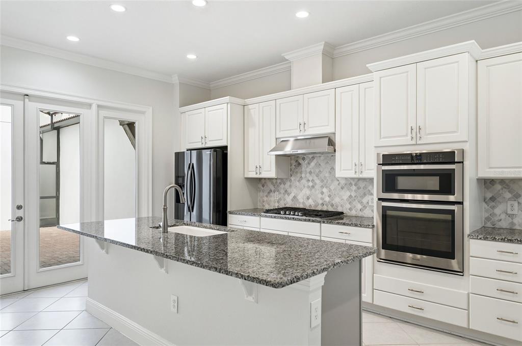 A modern kitchen features white cabinets, granite countertops, a center island, and stainless steel appliances — 8807 FOUNTAIN PALM ALY, WINTER GARDEN, FL