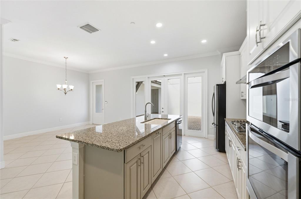 A kitchen with a granite-topped island, light cabinetry, stainless steel appliances, and tile flooring — 8807 FOUNTAIN PALM ALY, WINTER GARDEN, FL