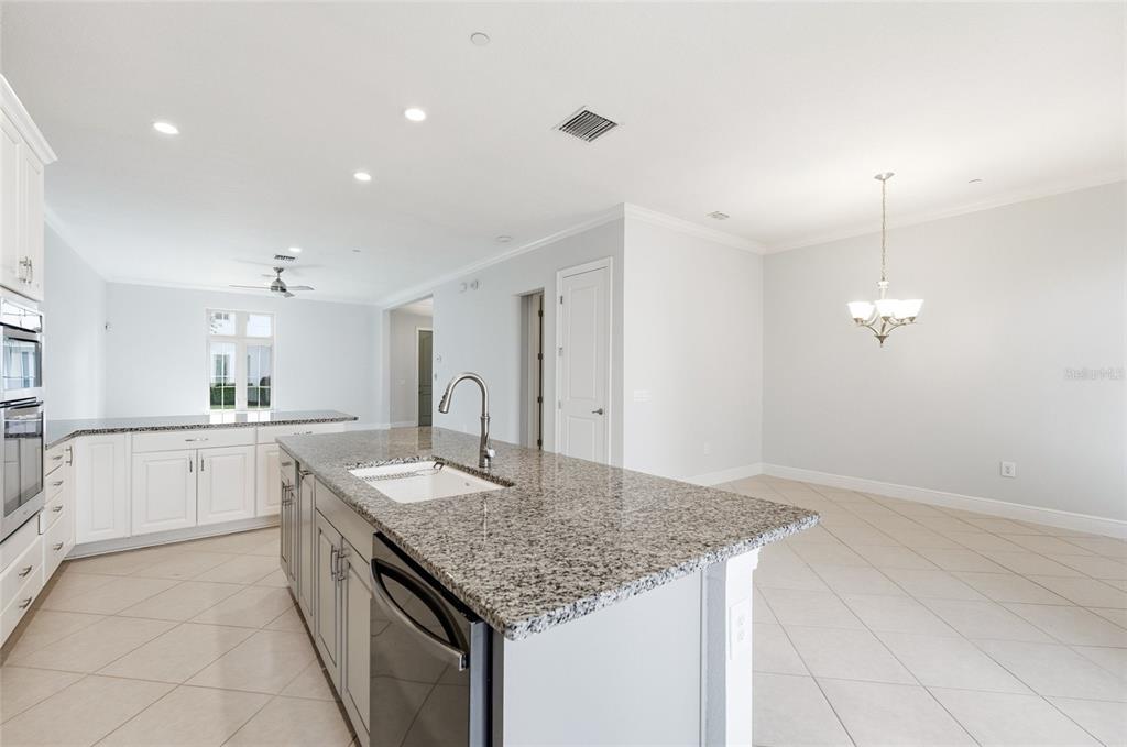 A kitchen with a granite-topped island, white cabinetry, and an adjacent dining area — 8807 FOUNTAIN PALM ALY, WINTER GARDEN, FL