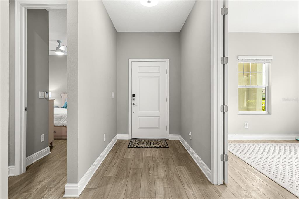 A bright entryway features light wood-look flooring, gray walls, and a white front door — 2918 BUTTERFLY JASMINE TRAIL, SARASOTA, FL