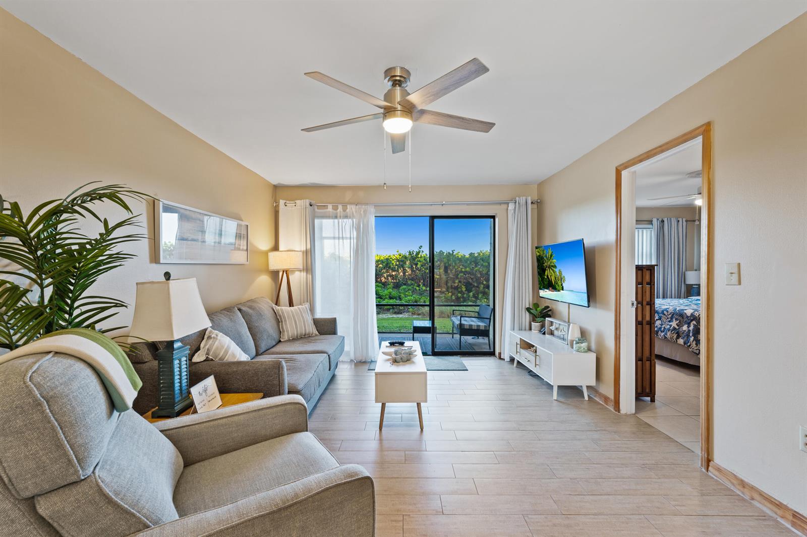 A living room with a grey sofa, armchair, ceiling fan, and sliding doors to a patio — 7420 S Ocean # 113, Jensen Beach FL 34957, JENSEN BEACH, FL