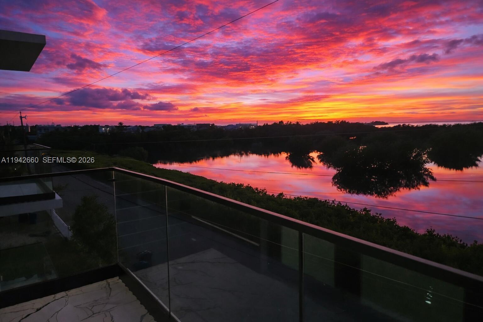 A balcony with a glass railing overlooks a lake reflecting a vibrant sunset — 141 Grassy Rd, Key Largo FL 33037, KEY LARGO, FL