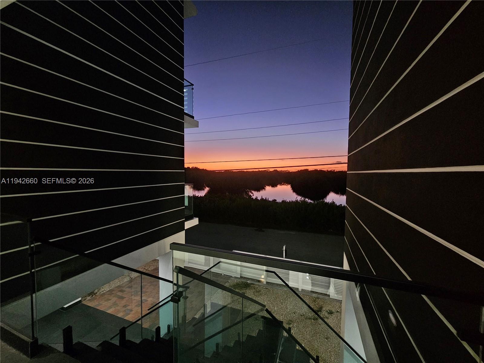 A view of a sunset over water framed by two modern buildings with glass railings — 141 Grassy Rd, Key Largo FL 33037, KEY LARGO, FL
