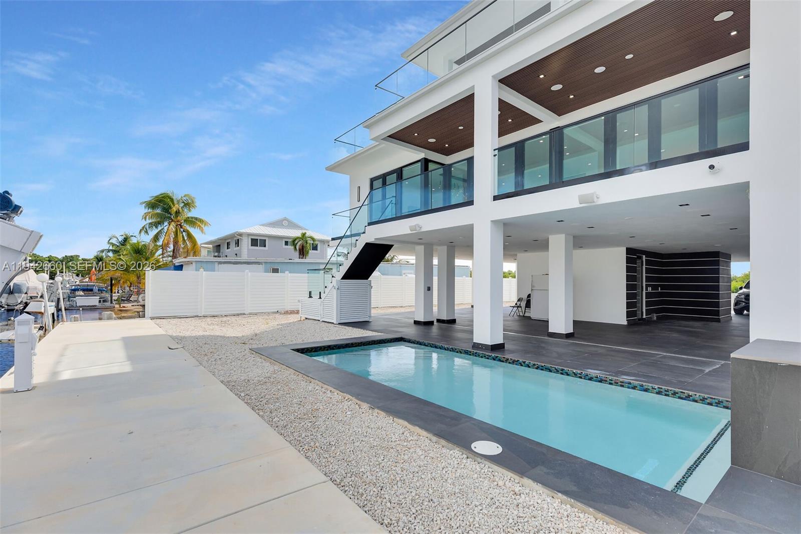 A modern elevated house features a rectangular swimming pool, a covered patio, and glass railings — 141 Grassy Rd, Key Largo FL 33037, KEY LARGO, FL