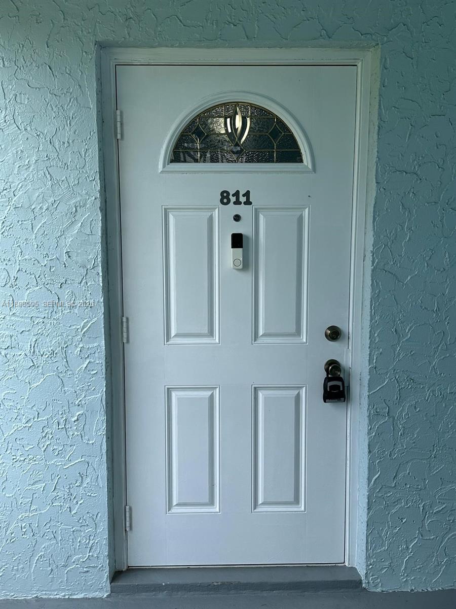 A white front door with a decorative glass arch, a smart doorbell, and house number 811 — 9848 Marina Blvd # 811, Boca Raton FL 33428, BOCA RATON, FL