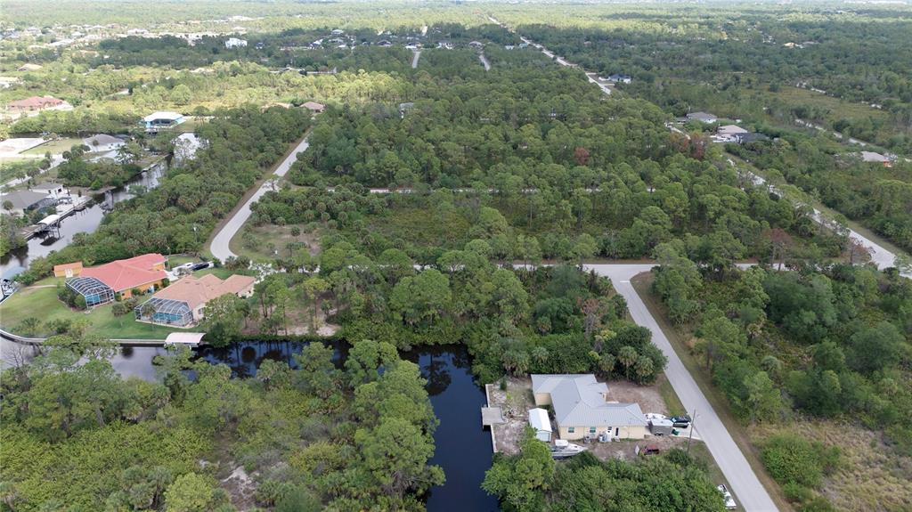 An aerial view shows houses along a canal surrounded by dense trees and paved roads — 13461 PULLEN AVENUE, PORT CHARLOTTE, FL