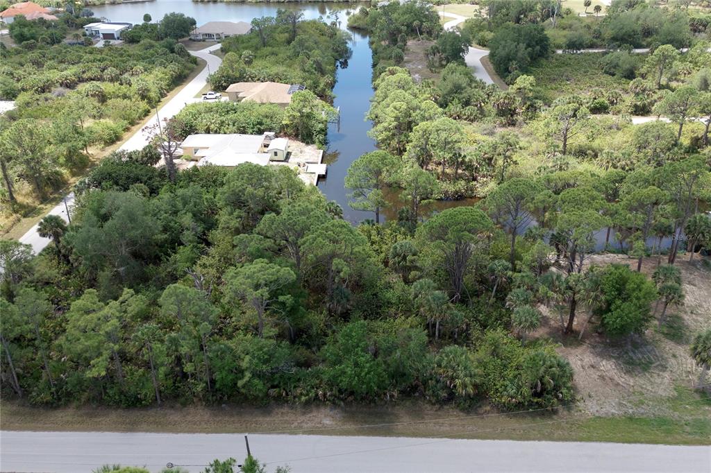 An aerial view shows a wooded waterfront lot with a canal and nearby houses — 13461 PULLEN AVENUE, PORT CHARLOTTE, FL