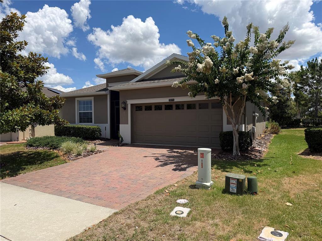 A single-story house with a brick paver driveway, a two-car garage, and a flowering tree — 3572 KINLEY BROOKE LANE, CLERMONT, FL