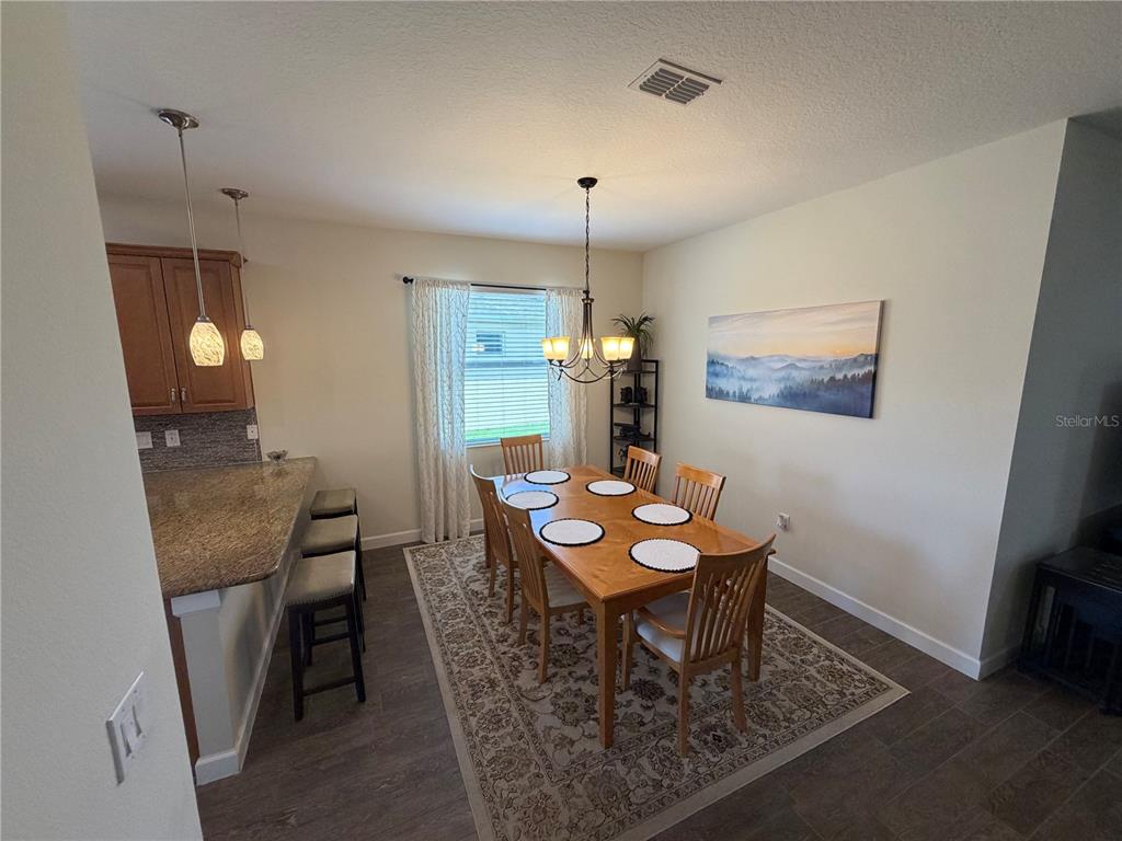 A dining area features a wooden table with six chairs, a rug, and pendant lighting — 3572 KINLEY BROOKE LANE, CLERMONT, FL