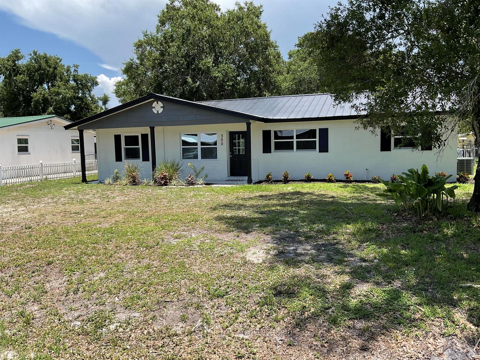 A single-story white house with a dark metal roof and black shutters sits on grass — 300 SE 15th Avenue, Okeechobee FL 34974, OKEECHOBEE, FL