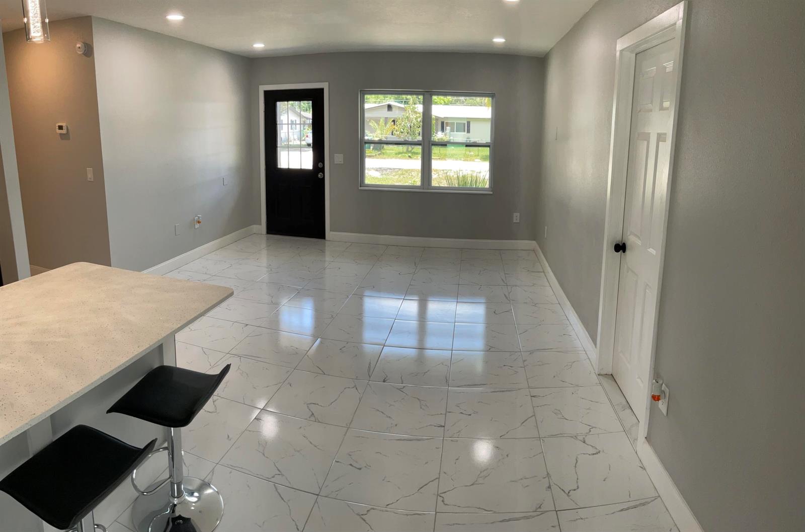 A bright, open-concept room features white marble-look tile flooring, light gray walls, and a black door — 300 SE 15th Avenue, Okeechobee FL 34974, OKEECHOBEE, FL